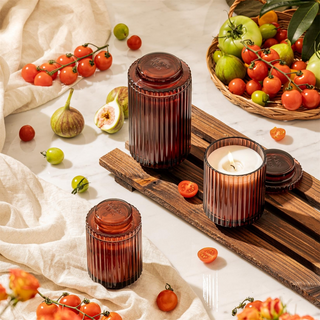 Two ribbed brown candles on a wooden tray with fresh fruits and vegetables on a light background