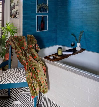Bathroom with blue tiled walls, a bathtub with a tray, and a robe on a chair.