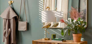 Room interior with coat, handbag, lamp, and plant against a light blue wall.