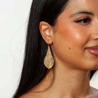 Close-up of a woman wearing gold earrings with a plain background